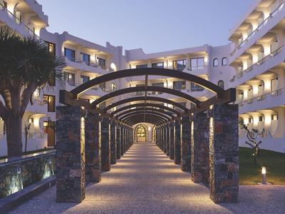 Osvětlená cesta s oblouky mezi hotelovými budovami a zahradou v noci.