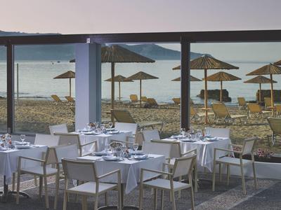 Restaurant met witte tafelkleden en stoelen met uitzicht op een strand met parasols en ligstoelen