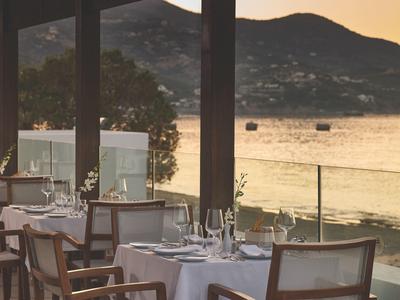 Elegant restaurant met witte tafelkleden en glazen voorkant met uitzicht op meer en bergen bij zonsondergang