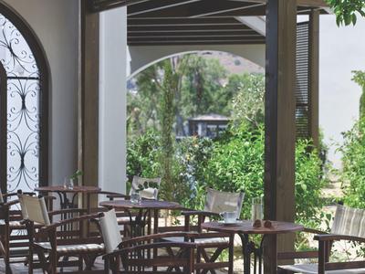 Open zitgedeelte van een café met houten tafels en stoelen naast een ruime tuin.