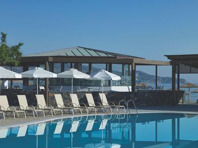 Outdoor-Pool mit Liegestühlen und Sonnenschirmen neben einem Gebäude mit Blick auf das Meer.