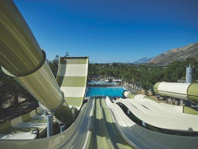 Několik tobogánů vede do velkého bazénu s čistou vodou pod modrou oblohou.