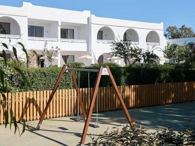 Kinderspeelplaats met schommel voor een wit hotelgebouw bij zonnig weer