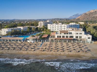 Ein Hotel mit großem Pool und vielen Sonnenschirmen am Sandstrand vor blauem Himmel.