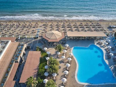 Luftaufnahme eines Hotels mit Pool, Liegestühlen und Sonnenschirmen am Strand.