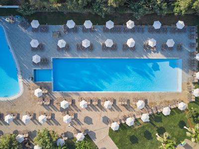 Vogelperspektive auf einen rechteckigen Hotelpool mit weißen Sonnenschirmen und Liegestühlen