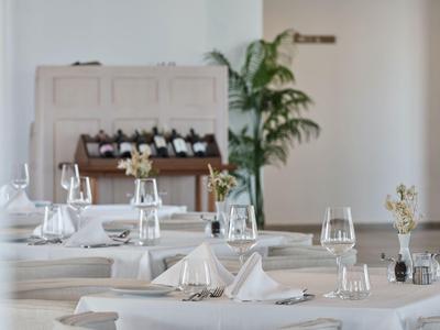 Eleganter Tisch mit weißen Tischdecken und Servietten in einem hellen Restaurant mit Pflanzen.