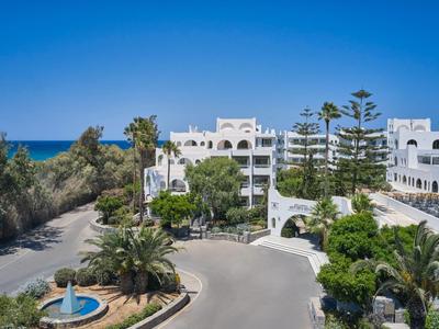 Weiße Hotelgebäude mit blauen Dächern vor Meer und klarem blauem Himmel