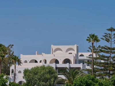 Weißes Hotelgebäude mit Bögen und Palmen im Vordergrund bei klarem Himmel.