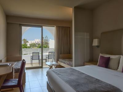 Modernes Hotelzimmer mit Kingsize-Bett, Schreibtisch und Balkon mit Blick auf Gebäude.