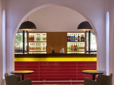 Moderner Hotelbarbereich mit rotem Tresen, beleuchteten Regalen und gemütlichen Sitzgelegenheiten.