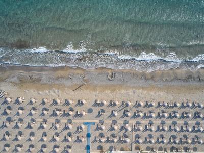 Luftaufnahme eines Strandes mit Reihen von Sonnenschirmen und klarer türkisfarbener Wasserlinie.