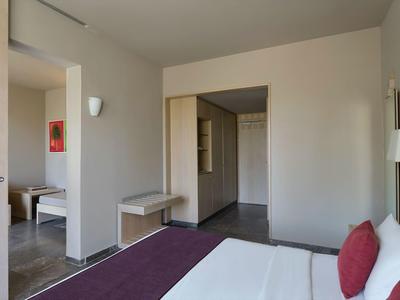 Helles Hotelzimmer mit Doppelbett, zusätzlicher Sitzbank und Zugang zu weiterem Raum.