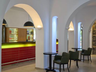 Moderner Barbereich mit roten Thekenfronten, grünen Sesseln und weißen Gewölbedecken.