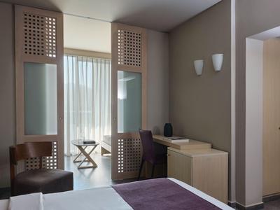 Modernes Hotelzimmer mit Zugang zu Balkon, Schreibtisch und Holzstühlen in natürlichen Farbtönen.