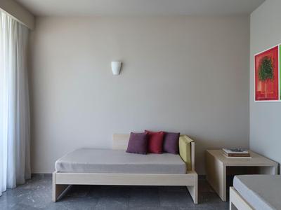 Modernes Hotelzimmer mit zwei Betten, beiger Wand, Nachttisch und buntem Kunstwerk.