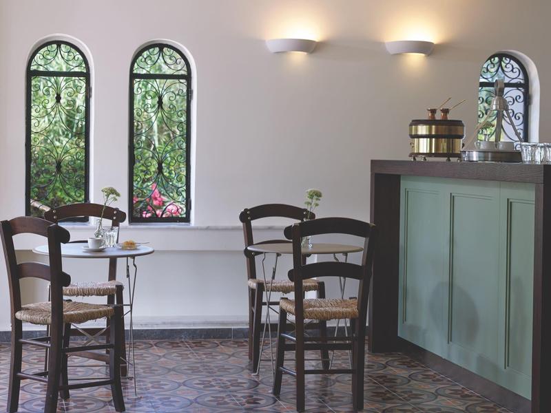 Gezellige binnenruimte van een café met houten tafels, stoelen en drie smalle boogramen.