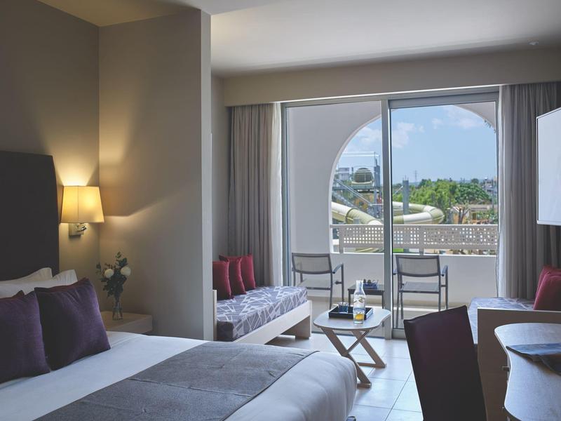 Hotelkamer met tweepersoonsbed, zithoek en balkon met uitzicht op daken en groene omgeving