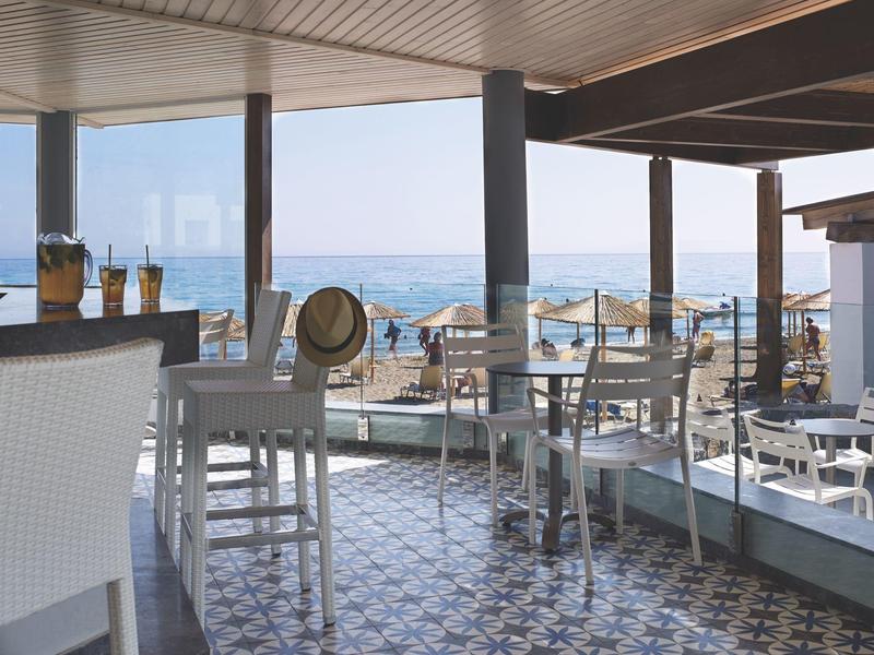 Terras van een strandcafé met uitzicht op de zee, tafels en stoelen, parasols op het strand.