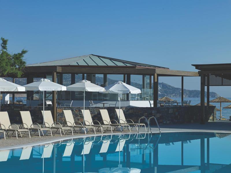 Buiten zwembad met ligstoelen en parasols naast een gebouw met uitzicht op zee.