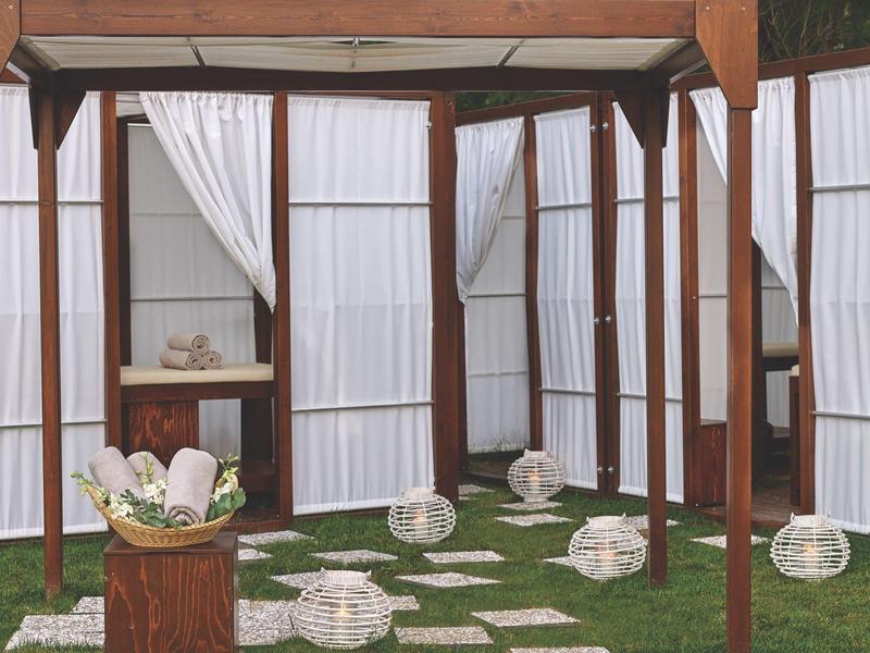 Buitenterras met witte lantaarns en decoratieve witte gordijnen op groen gras.