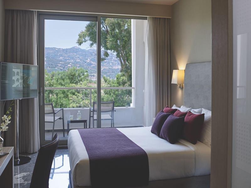 Modern hotelkamer met tweepersoonsbed en balkon met uitzicht op de bergen.