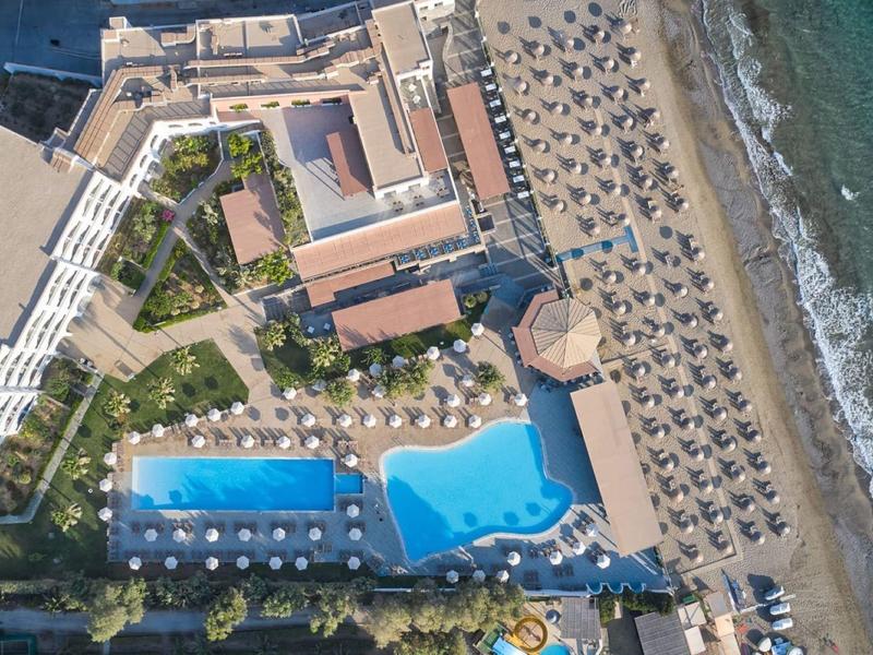 Luchtfoto van een hotel met zwembad, strandstoelen en directe toegang tot de zee.