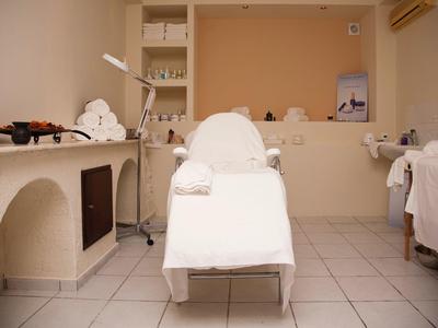 Prosto umeblowany pokój zabiegowy z leżanką i półkami z ręcznikami do zabiegów wellness.