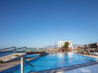 Large outdoor pool with sun loungers overlooking the sea and a building in the background.