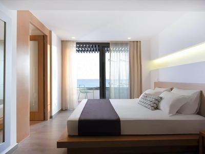 Modern hotel room with large bed, balcony, and sea view.