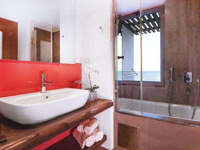 Nowoczesna łazienka z drewnianą półką, białą umywalką i wanną z widokiem na morze.