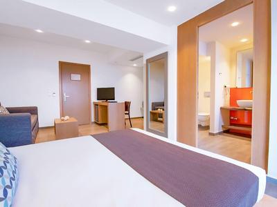 Nowoczesny pokój hotelowy z łóżkiem, sofą, telewizorem i szafą z lustrami.