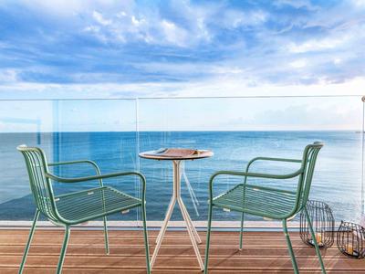 Dwa zielone krzesła i mały stolik na balkonie z widokiem na morze pod pochmurnym niebem.