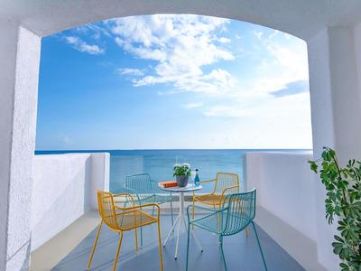 Balkon z kolorowymi krzesłami i stołem z kwiatami, widok na niebieskie morze pod niebieskim niebem.