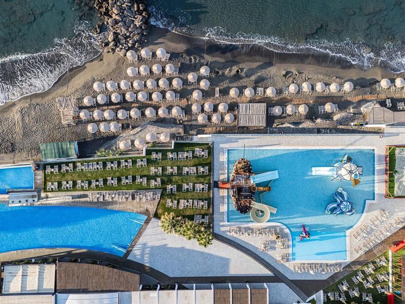 Widok z lotu ptaka na hotel z basenami, leżakami i bezpośrednim dostępem do morza.