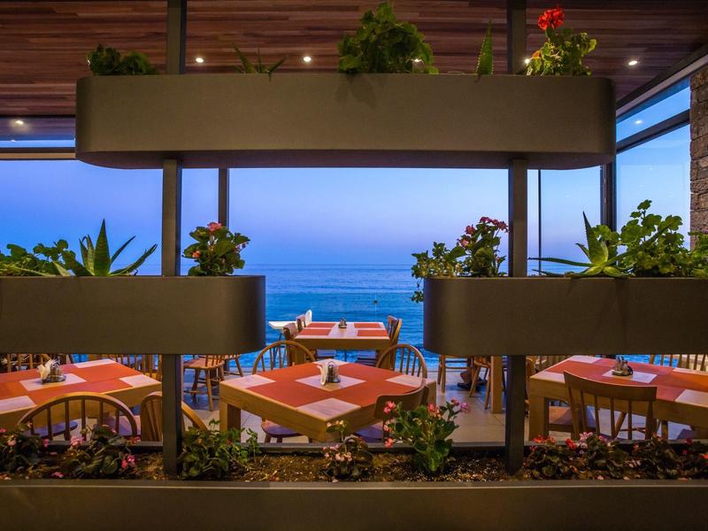 Taras z nakrytymi stołami z widokiem na morze o zachodzie słońca.