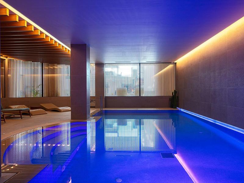 Nowoczesny basen kryty z niebieskim oświetleniem i leżakami w stylowym wnętrzu.