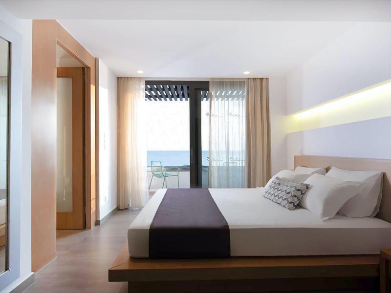 Nowoczesny pokój hotelowy z łóżkiem podwójnym, widokiem na morze i dużymi oknami z zasłonami.