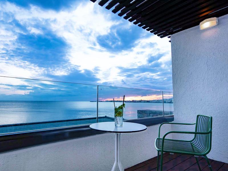 Balkon z krzesłem i stołem z widokiem na morze o zachodzie słońca.