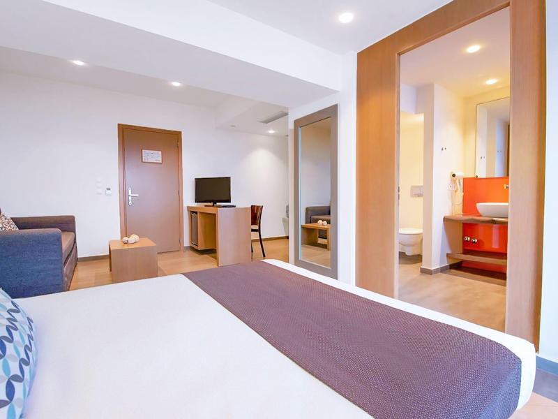 Nowoczesny pokój hotelowy z łóżkiem, sofą, telewizorem i szafą z lustrami.