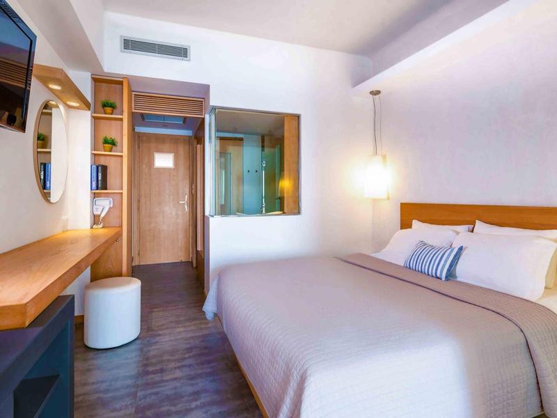 Nowoczesny pokój hotelowy z podwójnym łóżkiem, biurkiem, telewizorem i minimalistycznym wystrojem.