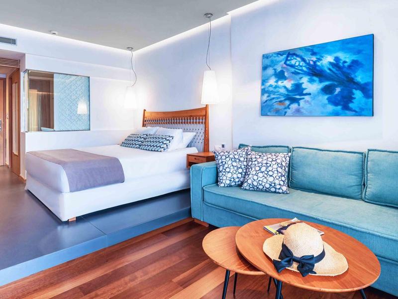 Nowoczesny pokój hotelowy z dużym łóżkiem, niebieską sofą i drewnianą podłogą.