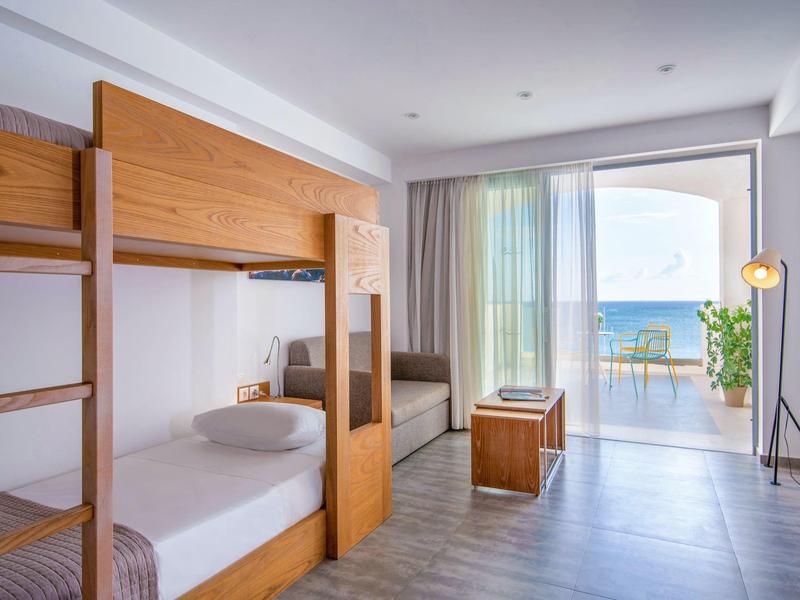 Nowoczesny pokój hotelowy z łóżkiem piętrowym, balkonem i widokiem na morze w świetle dziennym.