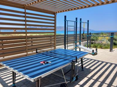 Tavolo da ping pong all'aperto su terrazza con vista sul mare e attrezzature per il fitness sullo sfondo.