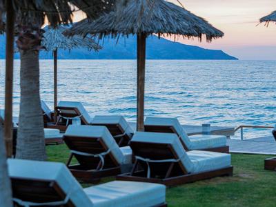 Lege ligstoelen onder rieten parasols met uitzicht op zee bij zonsondergang.