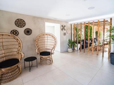 Area luminosa dell'hotel con sedie in vimini, piccoli tavoli e piante, atmosfera moderna.