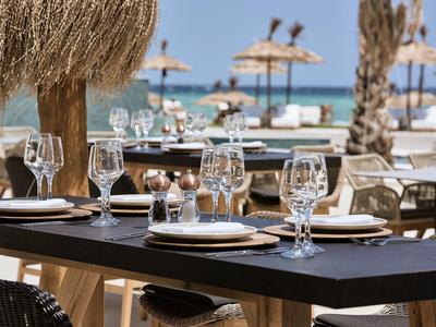 Tavolo apparecchiato con bicchieri sulla spiaggia sotto ombrelloni.