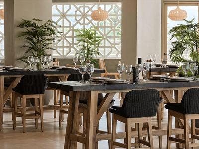 Area pranzo moderna con tavoli in legno, sedie nere e piante verdi in una stanza luminosa