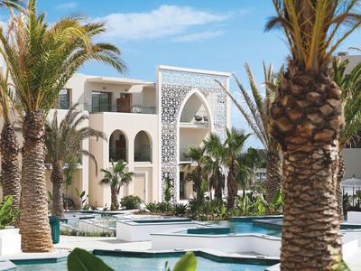 Luxuriöses Hotel mit Palmen, Pool und arabischer Architektur unter blauem Himmel.