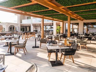 Zonnig buitenterras van een restaurant met tafels en stoelen onder een groen dak.